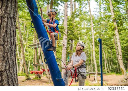 Mother and son climbing in extreme road trolley zipline in forest on carabiner safety link on tree to tree top rope adventure park. Family weekend children kids activities concept Portrait of a Mother and son climbing in extreme road trolley zipline in forest on carabiner safety link on tree to tree top rope adventure park. Family weekend children kids activities concept Portrait of a 92338551