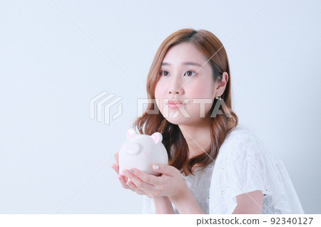 Young woman holding a piggy bank with both hands Young woman holding a piggy bank with both hands 92340127