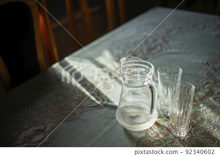 Three and empties. Selective focus on glass jug and glasses on the table. Sunset light. Blurred background. Three and empties. Selective focus on glass jug and glasses on the table. Sunset light. Blurred background. 92340602