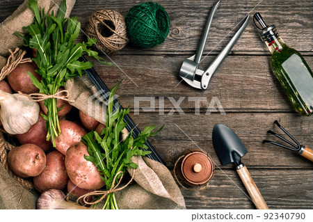 Raw potatoes in a linen bag, arugula, garlic, garden shovel and rake, food background, top view 92340790