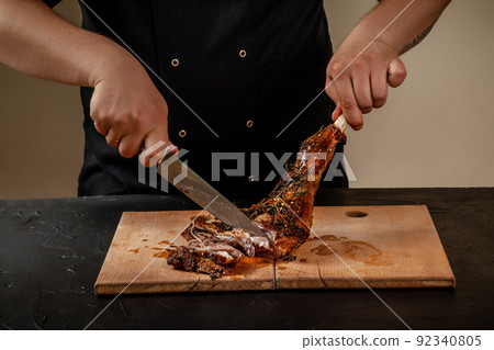 Chef is cutting roasted leg lamb on wooden board on table 92340805
