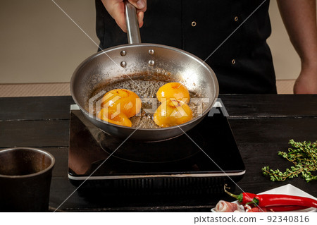 Peaches on a fry pan. Canned fruit yellow peaches, black wooden background, board. 92340816