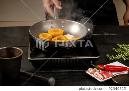 Peaches on a fry pan. Canned fruit yellow peaches, black wooden background, board. 92340825