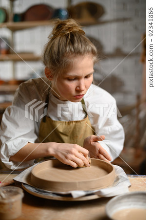 A ceramist makes a plate. Woman in an apron works in a pottery workshop.  92341866