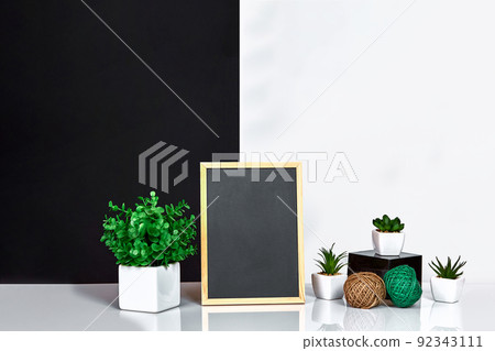 Wooden frame with black place for text. Mock up. Stylish room interior. Green plant in a white pot on black-white wall background Wooden frame with black place for text. Mock up. Stylish room interior. Green plant in a white pot on black-white wall background 92343111