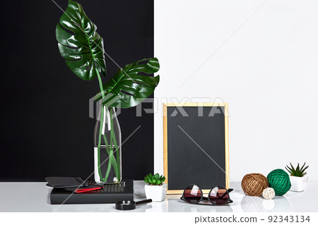 The stylish interior with mock up poster frame, leaves in glass bottle on table with black and white wall on background. The stylish interior with mock up poster frame, leaves in glass bottle on table with black and white wall on background. 92343134