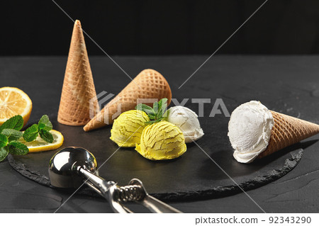 Tasty creamy and citrus lemon ice cream decorated with mint served on a stone slate over a black background. 92343290