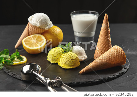 Tasty creamy and citrus lemon ice cream decorated with mint served on a stone slate over a black background. Tasty creamy and citrus lemon ice cream decorated with mint served on a stone slate over a black background. 92343292