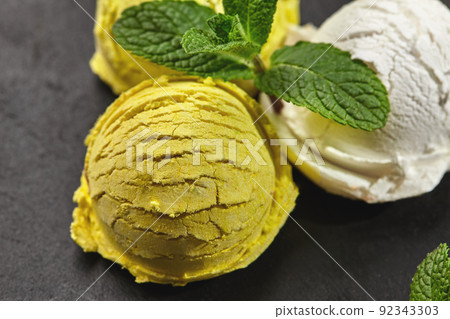 Tasty creamy and citrus lemon ice cream decorated with mint served on a stone slate over a black background. Tasty creamy and citrus lemon ice cream decorated with mint served on a stone slate over a black background. 92343303