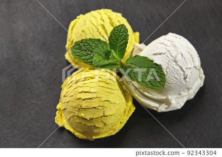 Tasty creamy and lemon ice cream decorated with mint served on a stone slate over a black background. Tasty creamy and lemon ice cream decorated with mint served on a stone slate over a black background. 92343304