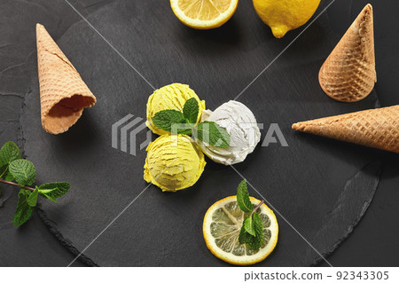 Tasty creamy and lemon ice cream decorated with mint served on a stone slate over a black background. 92343305