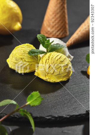 Tasty creamy and lemon ice cream decorated with mint served on a stone slate over a black background. 92343307