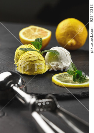 Tasty creamy and citrus lemon ice cream decorated with mint served on a stone slate over a black background. 92343318