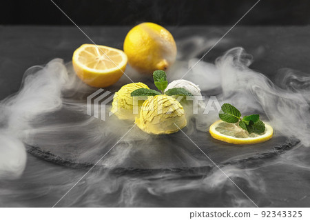 Tasty creamy and citrus lemon ice cream decorated with mint served on a stone slate over a black background. 92343325
