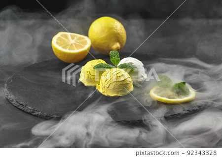 Tasty creamy and citrus lemon ice cream decorated with mint served on a stone slate over a black background. 92343328