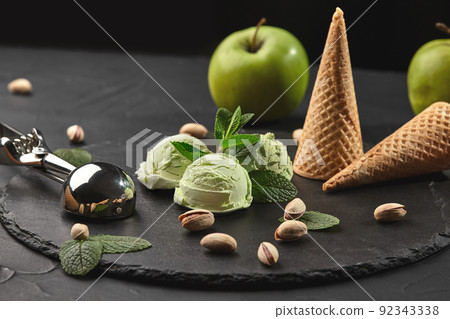 Gourmet pistachio ice cream served on a stone slate over a black background. 92343338