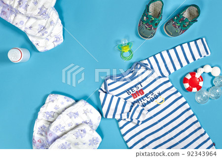 Babies goods: cloth diaper, baby powder, nibbler, cream, teether, soother, baby toy on blue background. Copy space. Top view. Babies goods: cloth diaper, baby powder, nibbler, cream, teether, soother, baby toy on blue background. Copy space. Top view. 92343964