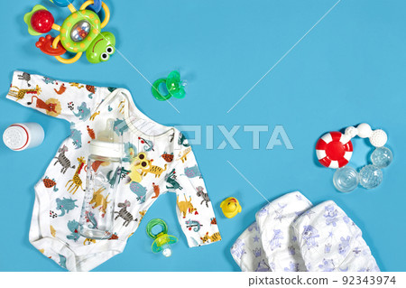 Babies goods: cloth diaper, baby powder, nibbler, cream, teether, soother, baby toy on blue background. Copy space. Top view. Babies goods: cloth diaper, baby powder, nibbler, cream, teether, soother, baby toy on blue background. Copy space. Top view. 92343974