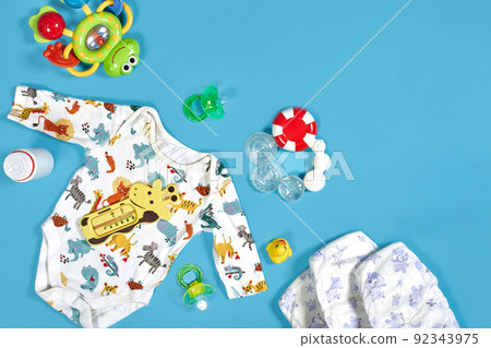 Babies goods: cloth diaper, baby powder, nibbler, cream, teether, soother, baby toy on blue background. Copy space. Top view. Babies goods: cloth diaper, baby powder, nibbler, cream, teether, soother, baby toy on blue background. Copy space. Top view. 92343975
