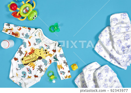 Babies goods: cloth diaper, baby powder, nibbler, cream, teether, soother, baby toy on blue background. Copy space. Top view. Babies goods: cloth diaper, baby powder, nibbler, cream, teether, soother, baby toy on blue background. Copy space. Top view. 92343977