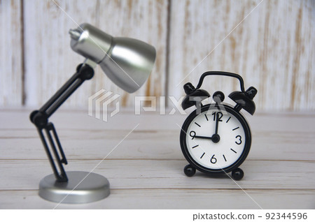 Alarm clock pointing at 9 o'clock with table lamp on wooden background. Copy space Alarm clock pointing at 9 o'clock with table lamp on wooden background. Copy space 92344596