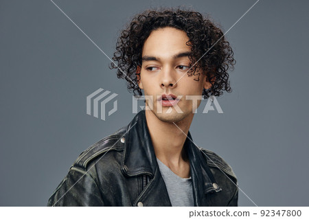 Pensive handsome stylish tanned curly man leather jacket looks aside posing isolated on over gray studio background. Cool fashion offer. Huge Seasonal Sale New Collection concept. Copy space for ad Pensive handsome stylish tanned curly man leather jacket looks aside posing isolated on over gray studio background. Cool fashion offer. Huge Seasonal Sale New Collection concept. Copy space for ad 92347800