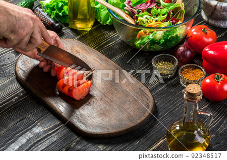 Man's hand cuts ripe red tomatoes for summer healthy vegetable salad on a wooden board, vertical 92348517