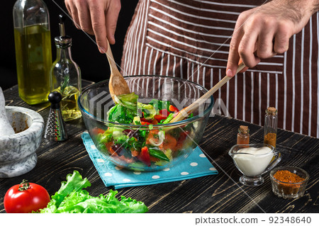 Man preparing salad with fresh vegetables on a wooden table. Cooking tasty and healthy food Man preparing salad with fresh vegetables on a wooden table. Cooking tasty and healthy food 92348640