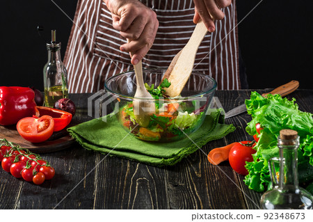Man preparing salad with fresh vegetables on a wooden table. Cooking tasty and healthy food Man preparing salad with fresh vegetables on a wooden table. Cooking tasty and healthy food 92348673