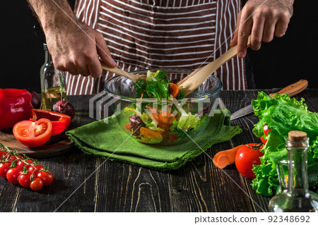 Man preparing salad with fresh vegetables on a wooden table. Cooking tasty and healthy food 92348692