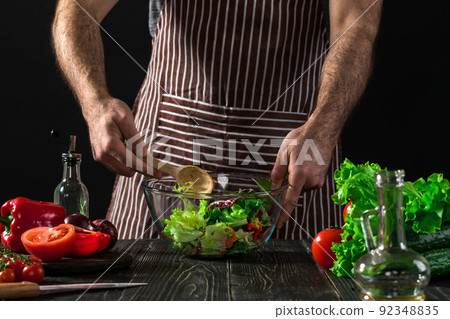 Man preparing salad with fresh vegetables on a wooden table. Cooking tasty and healthy food Man preparing salad with fresh vegetables on a wooden table. Cooking tasty and healthy food 92348835