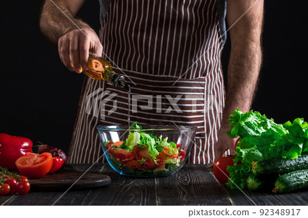 Cooking and home concept - close up of male hands flavouring salad in a bowl with olive oil Cooking and home concept - close up of male hands flavouring salad in a bowl with olive oil 92348917
