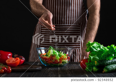 Man preparing healthy salad of fresh vegetables on a wooden table. Man preparing healthy salad of fresh vegetables on a wooden table. 92348932