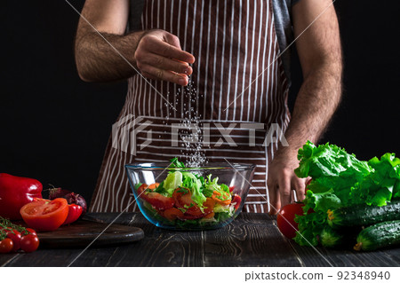 Man preparing healthy salad of fresh vegetables on a wooden table. 92348940