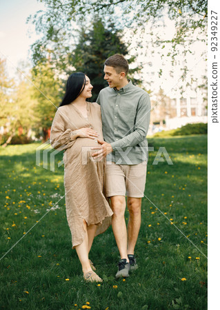 Pregnant woman and her husband standing in a park on a grass and hugging 92349227