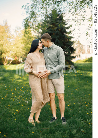 Pregnant woman and her husband standing in a park on a grass and hugging 92349228