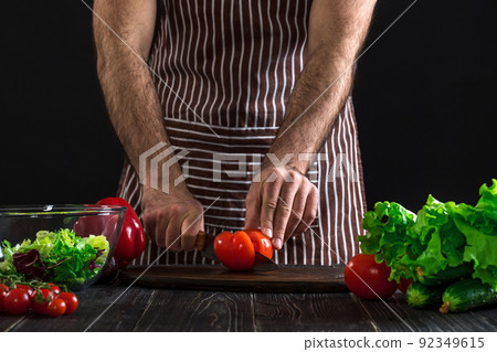 Man preparing salad on a wooden table. Men's hands cut the tomato to make a salad on black background Man preparing salad on a wooden table. Men's hands cut the tomato to make a salad on black background 92349615