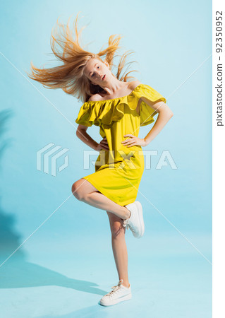 Studio shot of young beautiful blonde in summer yellow dress isolated on light blue background. Concept of beauty, art, fashion, human emotions 92350952