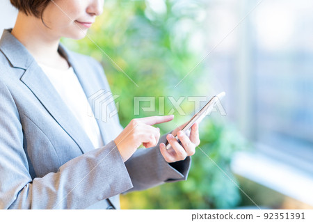 一位女士(部分)在辦公室窗戶附近操作智能手機 一位女士(部分)在辦公室窗戶附近操作智能手機 92351391