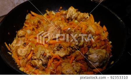 Homemade Korean Spicy chicken dish, frying chiken with carrot in a pan with sunflower oil. 92353310