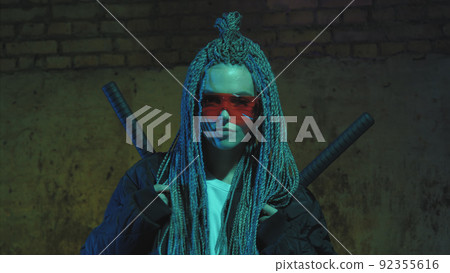girl with dreadlocks and katanas in red glasses posing against a neon brick wall 92355616