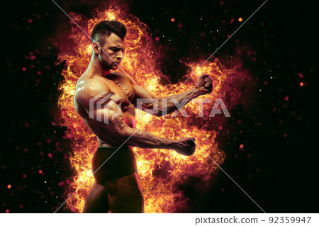 Brutal strong athletic Bodybuilder posing. Fire and spark explosion in the background. 92359947
