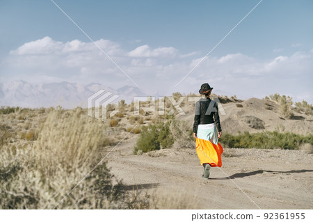 rear view of an asian woman in long skirt walking on a dirt road through gobi desert 92361955
