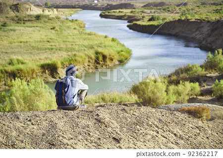 rear view of male asian photographer sitting on top of a hill looking down at a river rear view of male asian photographer sitting on top of a hill looking down at a river 92362217