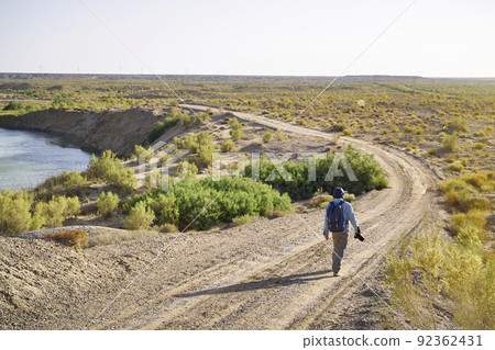 asian man photographer walking on dirt road in gobi desert looking at landscape at sunset 92362431