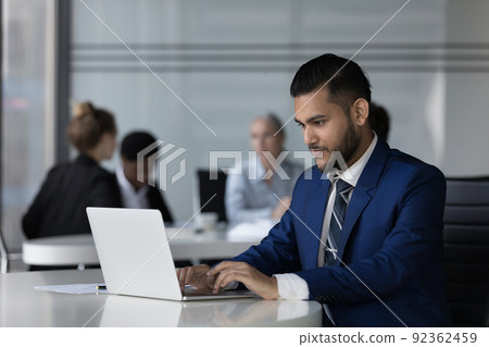 Focused Indian employee man working on online project at laptop Focused Indian employee man working on online project at laptop 92362459