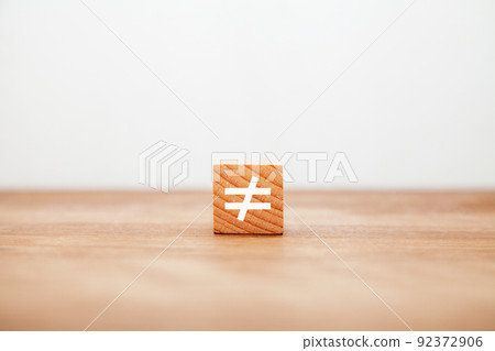 Not equal symbol. ≠. Not equal. Written on a wooden block. White letters. Wooden table background. 92372906