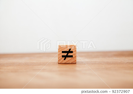 Not equal symbol. ≠. Not equal. Written on a wooden block. Black letters. Wooden table background. 92372907
