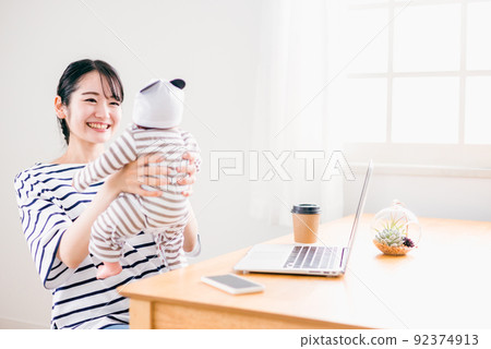 在家抱著嬰兒遠程工作的女性(育兒/看護) 在家抱著嬰兒遠程工作的女性(育兒/看護) 92374913