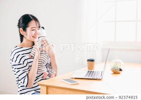 A woman who teleworks while holding a baby at home (working from home) 92374915
